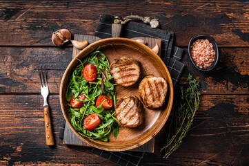 Roasted pork medallions steaks from tenderloin fillet with vegetable salad in wooden plate. Wooden background. Top view