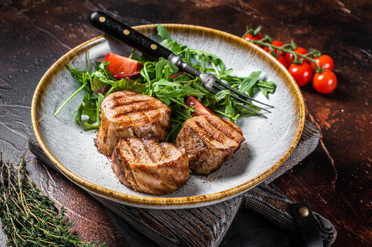 Grilled pork medallions steaks, tenderloin fillet with salad in plate. Dark background. Top view