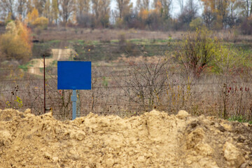 Close-up view of a caution banner, mock-up of a blue plate on an iron mesh fence with barbed wire....