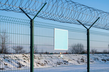 Close-up view of a caution banner, mock-up of a blue plate on an iron mesh fence with barbed wire. Closed area designation blank. Limited movement, lockdown and closed territory concept