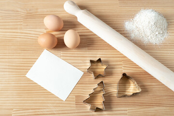 Homemade Christmas cookies. Blank greeting card or business card on wooden work table. Rolling pin, cookie cutters, eggs. Template for recipes.Top view, flat lay