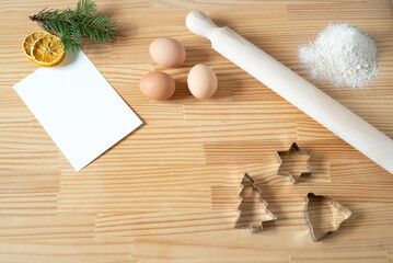 Homemade Christmas cookies. Blank greeting card or business card on wooden work table. Rolling pin, cookie cutters, eggs. Template for recipes.Top view, flat lay