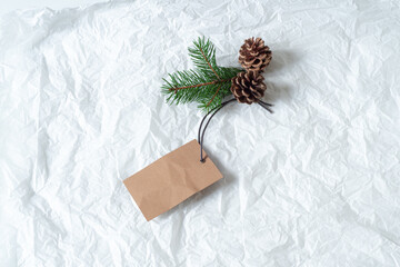 Close up of green fir branch and pine cones with blank white label. Price tag mockup scene on tissue paper background. Christmas composition, top view, flat lay
