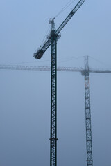 Two cranes working in a foggy afternoon