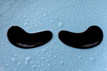 Black under eye patches on light blue wet background, closeup. Cosmetic product