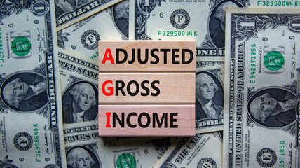 AGI adjusted gross income symbol. Concept words AGI adjusted gross income on wooden blocks. Beautiful background from dollar bills, copy space. Business and AGI adjusted gross income concept.