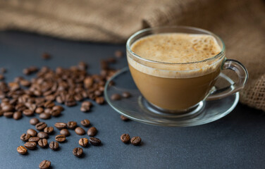 hot delicious aromatic cappuccino coffee in a glass transparent cup on a background of coffee beans