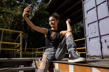 latina woman (20) sitting on the edge of a staircase with cell phone in hand taking a picture. Technology concept