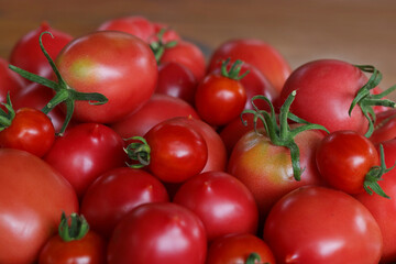 Background of beautiful and red tomatoes in basket. Tomato harvest. Top view. Fresh ripe organic juicy delicious tomatoes on wooden background. Healthy eating, vegetarianism, vegan