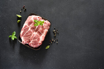 Fresh raw pork. Meat steaks in black lost with basil on a concrete background. Advertising.
