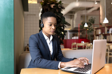 Serious African American woman uses a headset for a video call, works in a cafe, during a tourist business trip, business woman focused and thoughtful at work