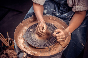 Young and cheerful woman shows how to work with clay and pottery wheel. Close-up.