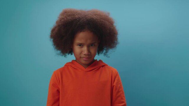 Cute African American girl shaking her head negative saying 'No' standing on blue background. Kid disagrees by moving her head.