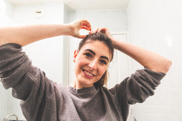 Mirror point of view of a young caucasian woman doing a ponytail in the bathroom.