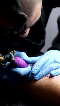 4k vertical video of Man tattooing a woman's leg in a tattoo studio