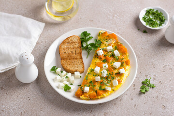 Scrambled eggs omelet with pumpkin and feta on a white plate with toast and herbs on beige textured background. Delicious homemade breakfast