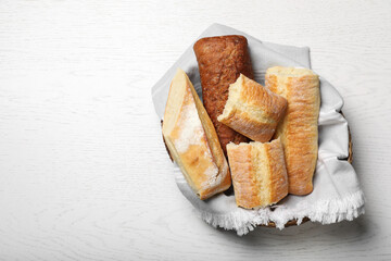 Different tasty baguettes in basket on white wooden table, top view. Space for text