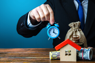 A man holds an alarm clock over the house and money. Limited offer. Rental business. Favorable...