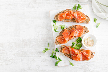 Whole grain rye bread open sandwiches with salted salmon on a white rustic wooden table. Healthy...