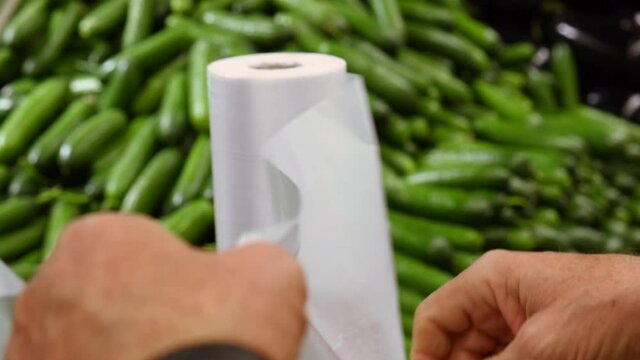 the buyer tear off a plastic bag in a supermarket against the background of a vegetable shop with fresh cucumbers. slow motion. High quality 4k footage