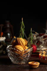 cookies in the form of nuts, with cream filling in a glass bowl, decorated with rosemary Christmas trees. Close-up, low key