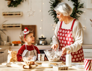 Cute little boy helping senior grandmother to make dough for traditional Christmas cookies
