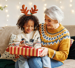 Happy afro american curly boy sitting on grandmother lap with christmas present, smiling at camera