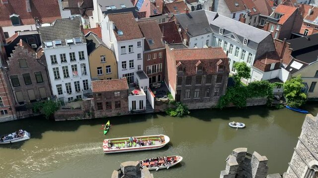 Tourist boats are crossing Leie river, canal next to the Graslei Quay. People in kayak and floating boat. View from Gravensteen medieval ages castle. Ghent, East Flanders, Belgium