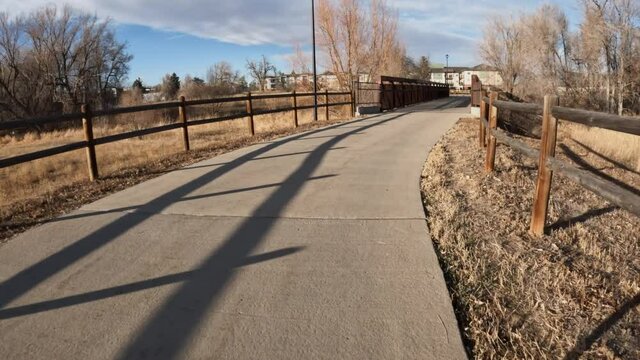 First person POV with a cyclist shadow from riding a touring bike on a paved urban trail in Fort Collins, Colorado, late fall scenery