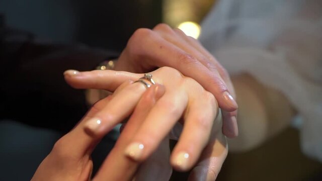 Bride and groom exchange wedding rings at ceremony close up. Put on finger jewelry symbol of love and togetherness. Man and woman in love. Marriage indoors.