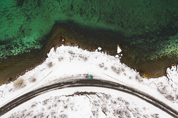Winter season aerial top down view of coastline road on Lofoten in Norway. Cold picture with clear green and blue ocean and camper van car on parking lot.
