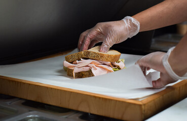 Restaurant kitchen employee wrapping freshly made sandwich for customer takeout order