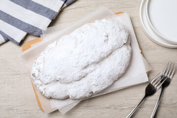 Delicious Stollen sprinkled with powdered sugar on wooden table, flat lay