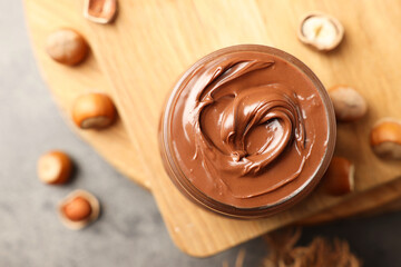 Tasty chocolate hazelnut spread and nuts on wooden board, flat lay. Space for text