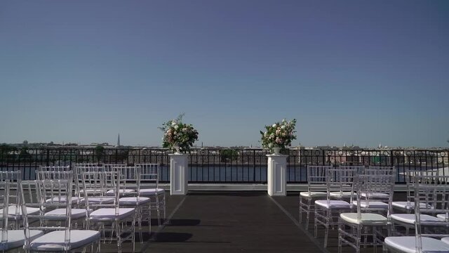 Decorated wedding ceremony outside in summer on rooftop. Wedding arch with white and pink rose flowers. White Chiavari chairs.
