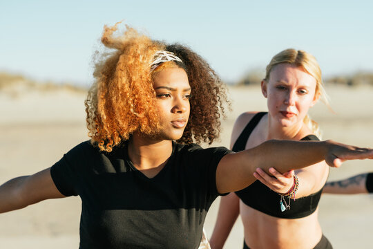 Yoga instuctor correcting the pose of a pregnant woman during a class on a beach - Powered by Adobe