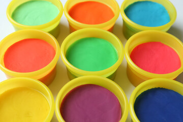 Plastic containers with colorful play dough on white background, closeup