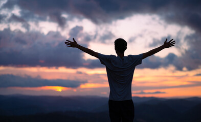 Young man with his arms raised with sunset in the background. Freedom, success and happiness concept.