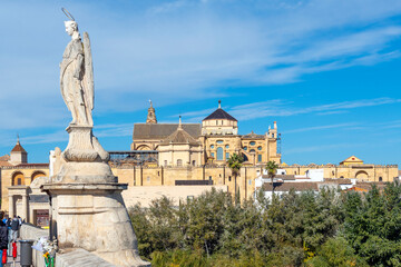 Fototapeta na wymiar The statue of Archangel Raphael on the ancient Roman Bridge with the Mezquita Mosque Cathedral and town of Cordoba Spain in view. 