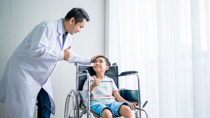 Obraz premium Male doctor standing, caring and cheering for a boy patient sitting in a wheelchair by the window.