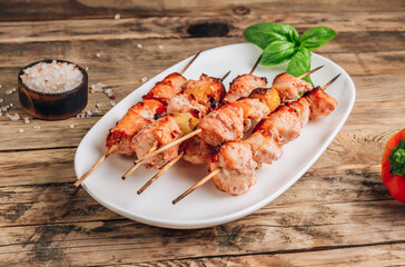Grilled chicken on bamboo skewers with basil on rustic wooden background.