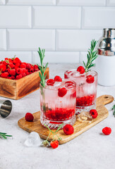 Raspberry lemonade in a glass with ice and fresh rosemary on a stone background.