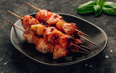 Grilled chicken on bamboo skewers with basil on black background. Selective focus