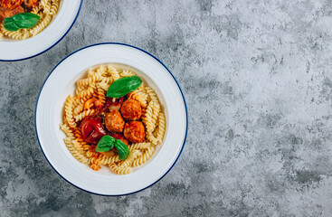 Pasta Fusili with meatballs, tomato and basil in two bowls on concrete background