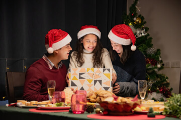 Daughter surprises and delights while opening gift boxes at Christmas with mom and dad