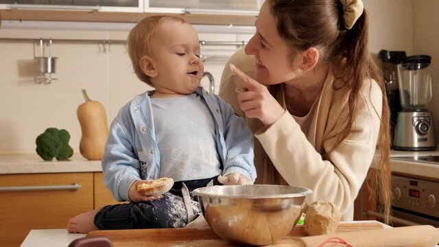 Happy smiling mother with baby son playing on kitchen with flour while cooking bread. Concept of little chef, children cooking food, healthy nutrition.