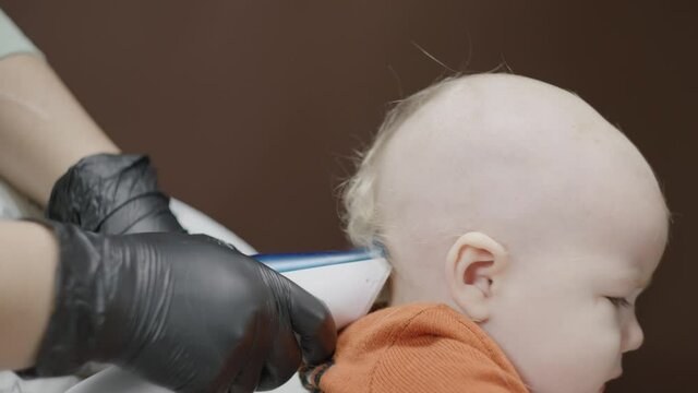 the master cuts the hair on the back of a one-year-old baby's head