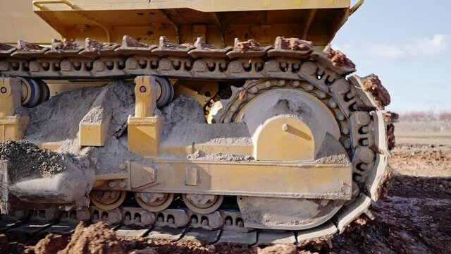 Tracking shot of crawler bulldozer working on construction site or quarry. Mining machinery moving clay, smoothing gravel surface for new road. Earthmoving, excavations, digging on soils.