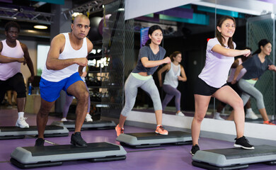 Fototapeta na wymiar Sporty women and men doing cardio exercises training with step platforms at fitness center