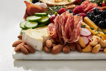 Cheese board with cold cuts, fruit and vegetables on a white background
